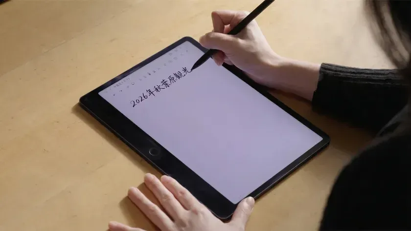 机の上で、一人の人物がデジタルペンを使ってタブレットに手書きで書き込んでいる様子。